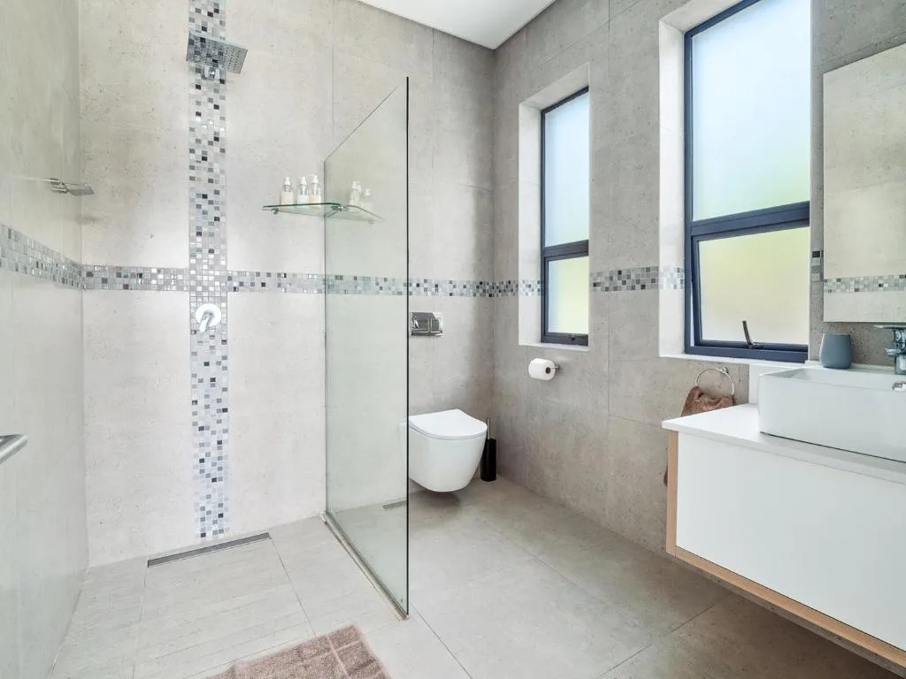 Modern bathroom with walk-in shower, white vanity, and bright windows