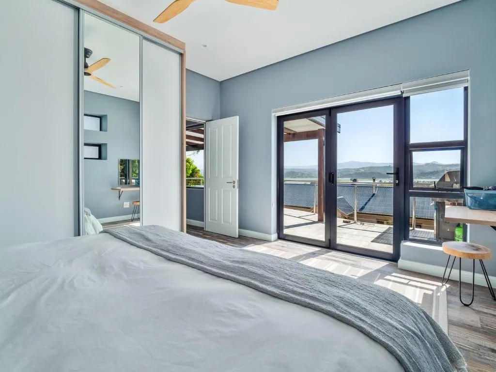 Bright bedroom with bed, mirror, and glass doors opening to mountain views