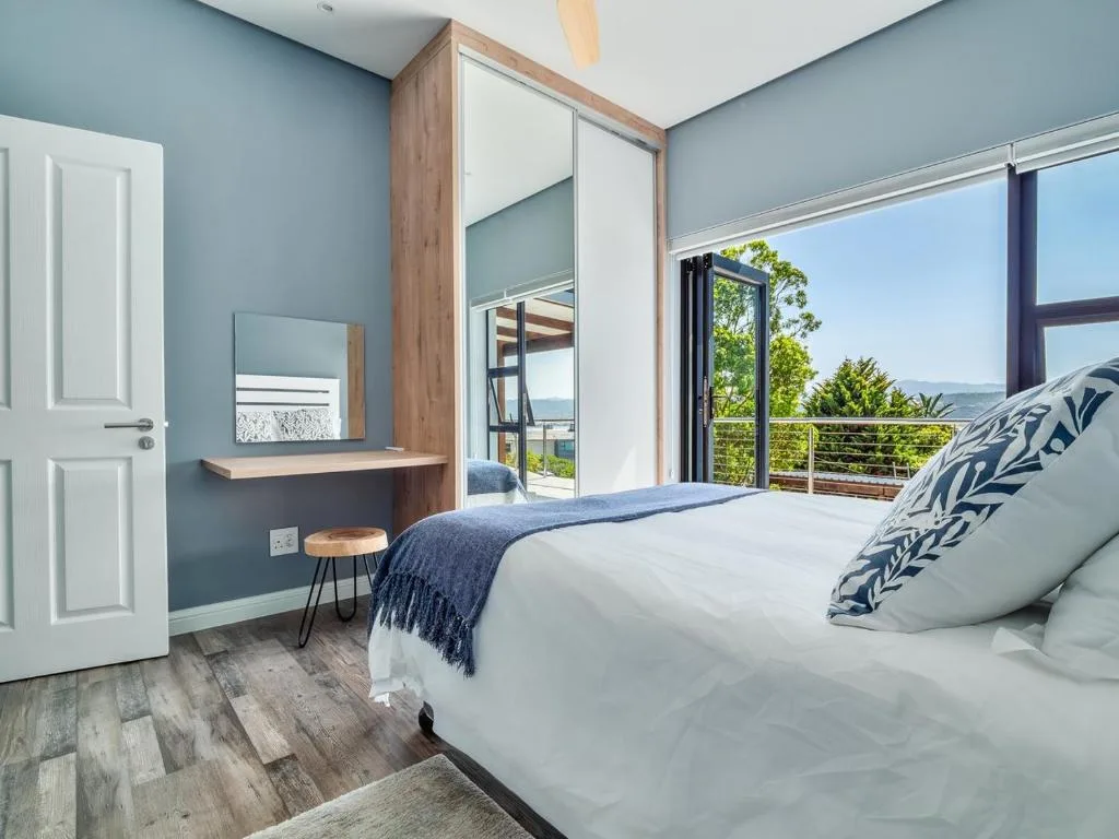 Modern bedroom with mountain views through large glass doors and deck access