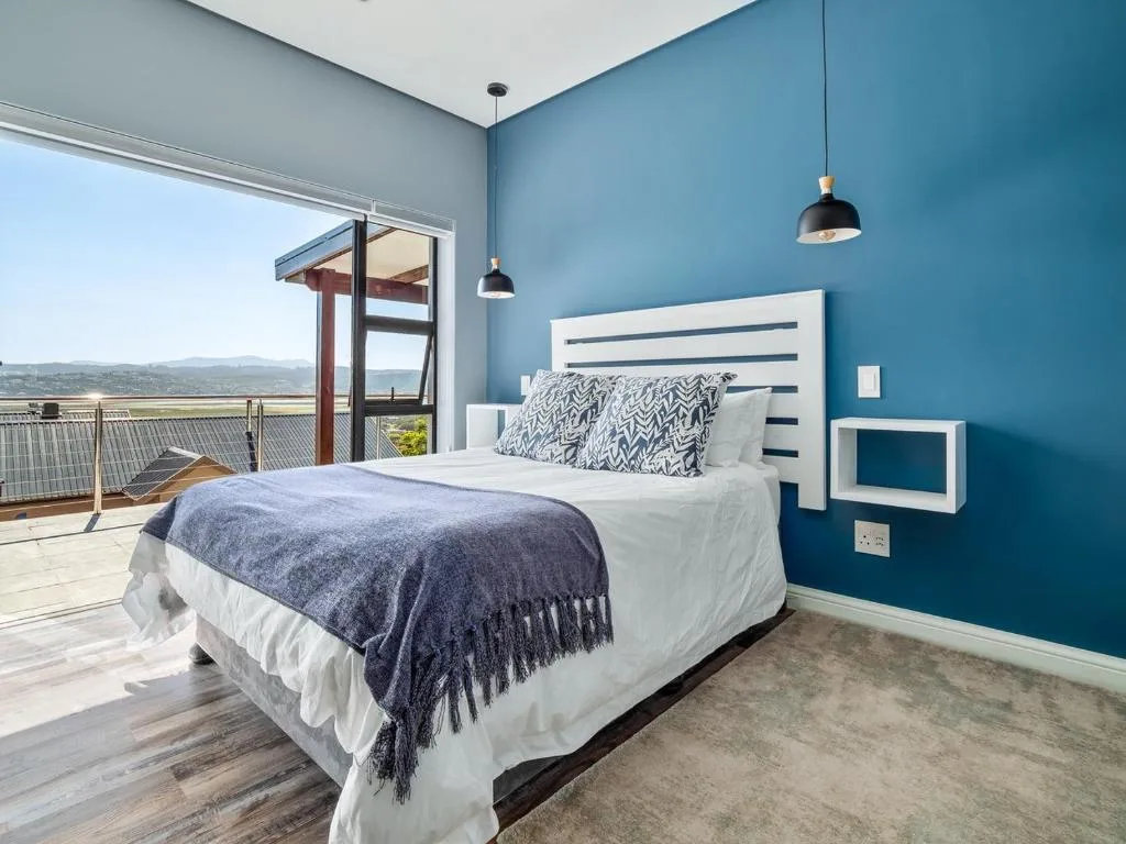 Modern bedroom with blue walls, white bedding, and scenic valley views from deck