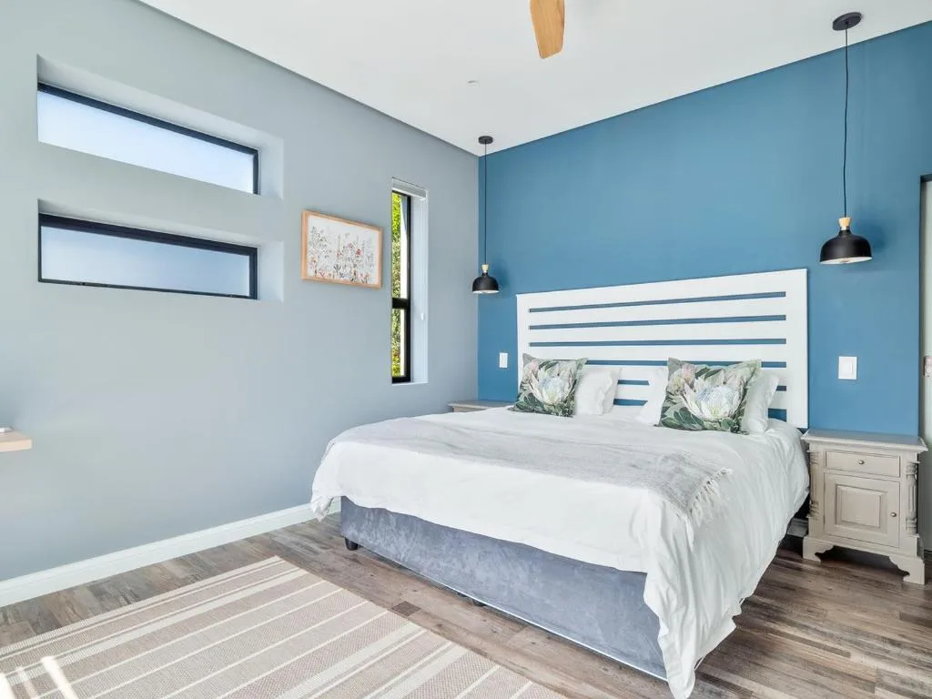 Modern bedroom with blue accent wall, striped headboard, and pendant lights