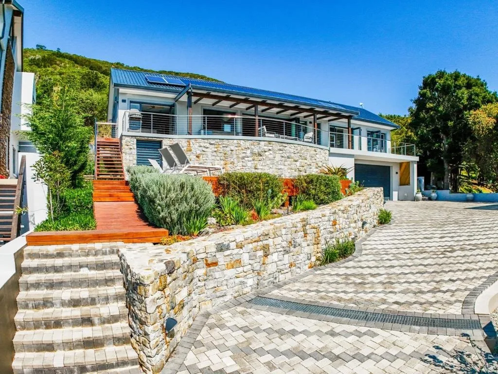 Modern stone and white home with blue roof and manicured gardens on hillside