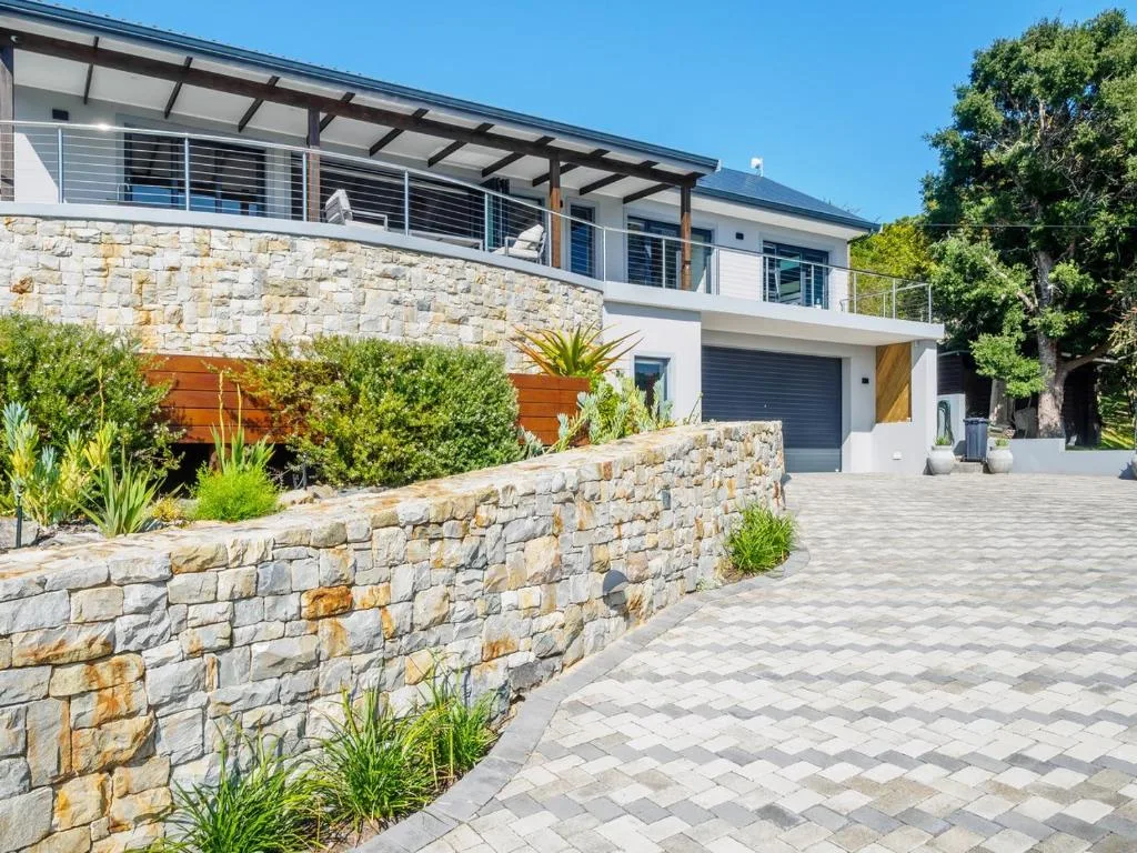 Modern two-story house with stone walls, upper deck, and paved driveway