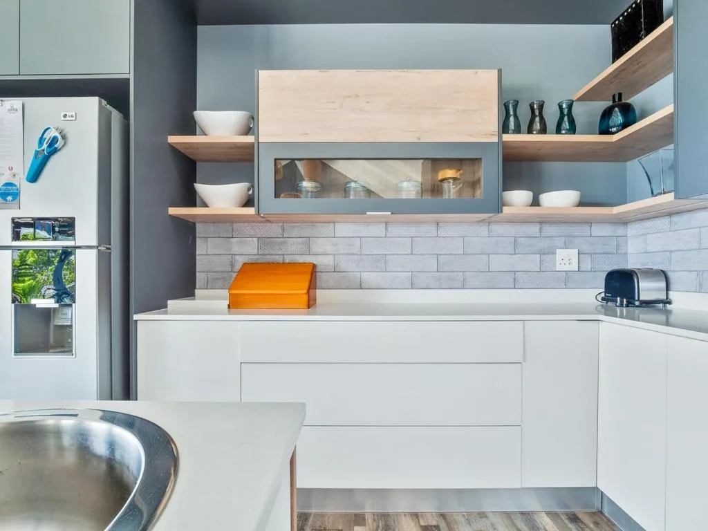 Modern kitchen with white cabinetry, light blue walls, and wooden shelves displaying dinnerware