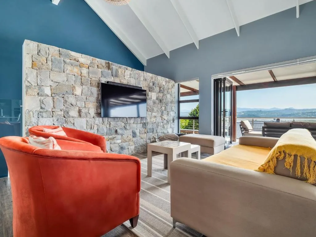 Modern lounge with red chair, beige sofa, stone fireplace and lagoon view