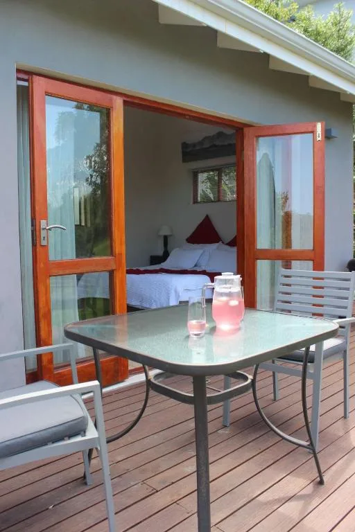 Wooden deck with dining table overlooking bedroom through red-framed doors