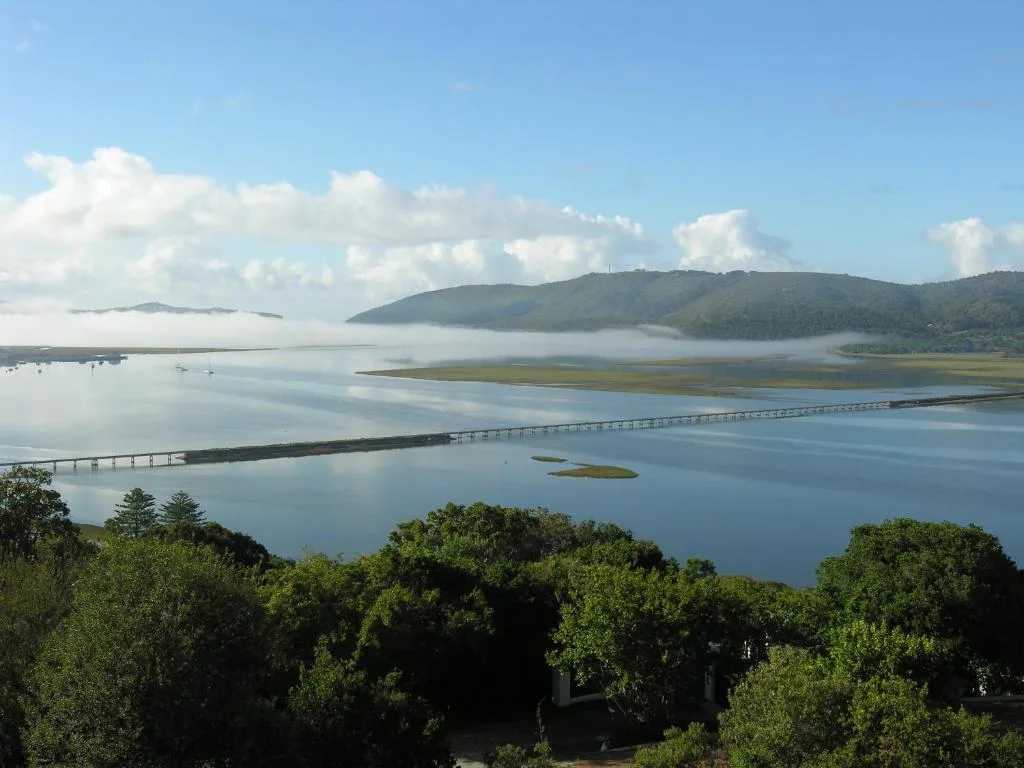 Scenic lagoon view with forested mountains and causeway bridge under blue sky