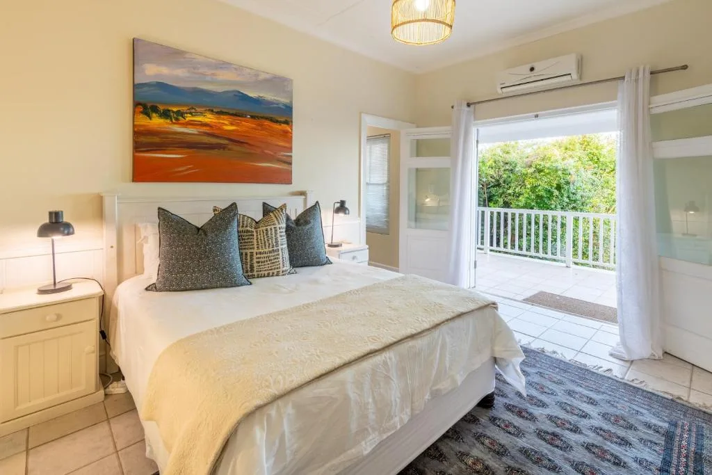 Bright bedroom with queen bed, decorative pillows, landscape artwork, and balcony access