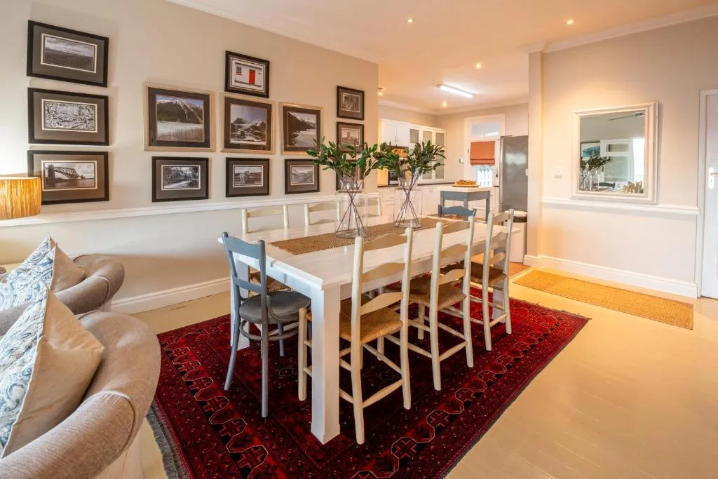 Spacious dining area with white table, framed landscape photos, and red rug