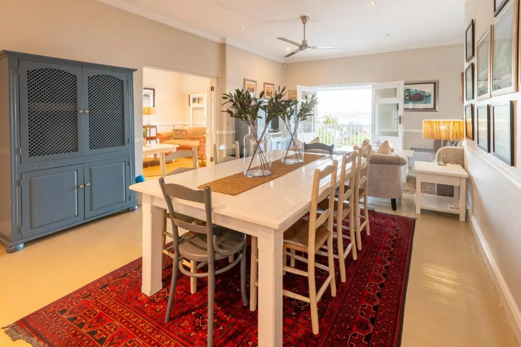 Spacious dining room with white table, wooden chairs, fresh flowers, and red rugs
