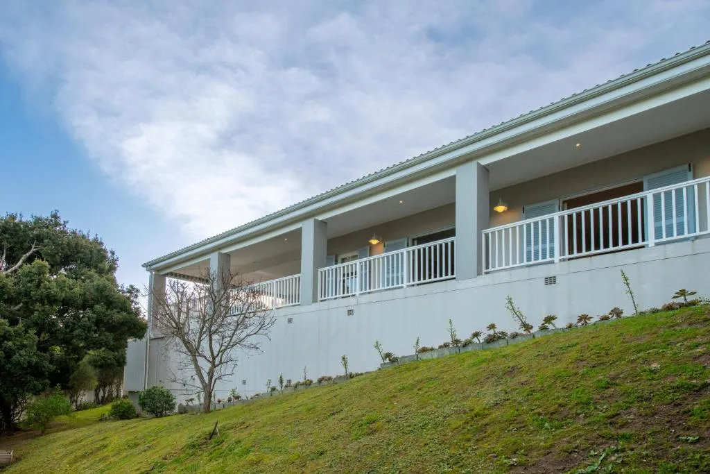 Modern white house with covered deck and manicured green lawn slope