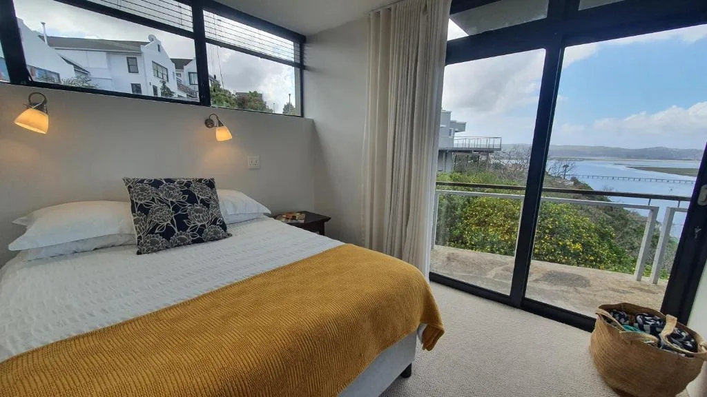 Modern bedroom with queen bed overlooking lagoon and mountains through floor-to-ceiling windows