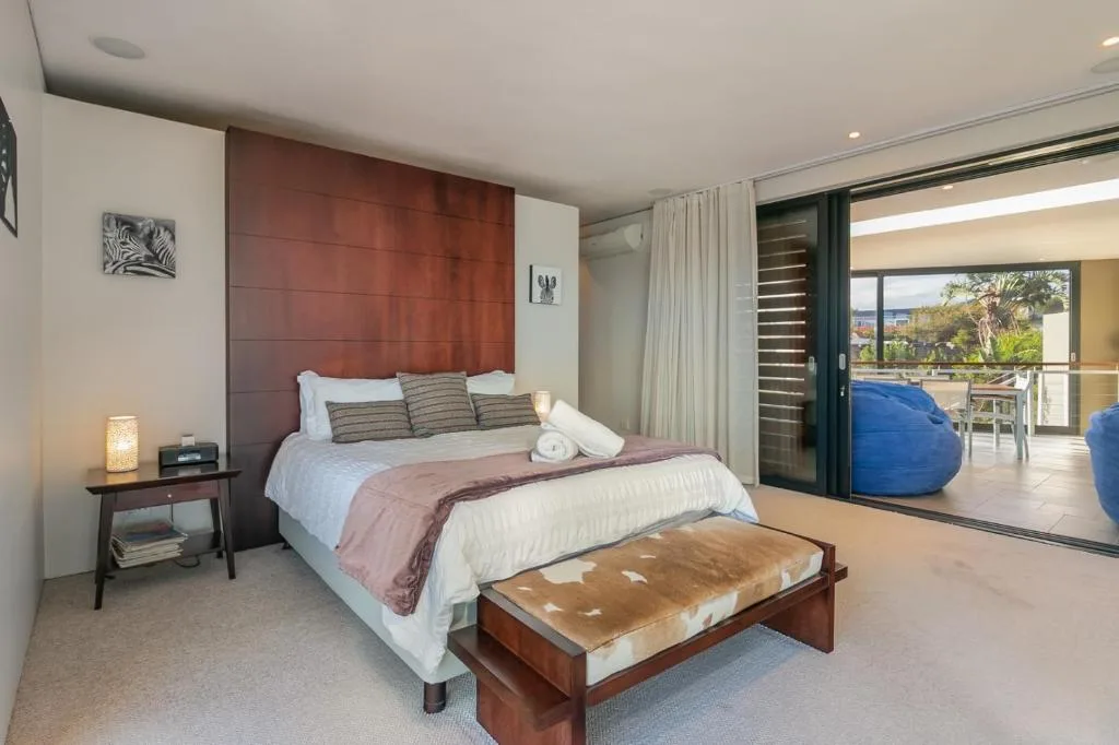 Modern bedroom with wooden headboard, white bedding, and deck access beyond