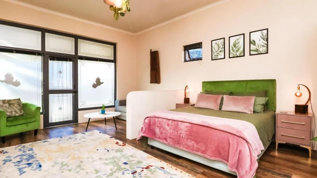 Bright bedroom with green headboard, pink bedding, and garden views through doors