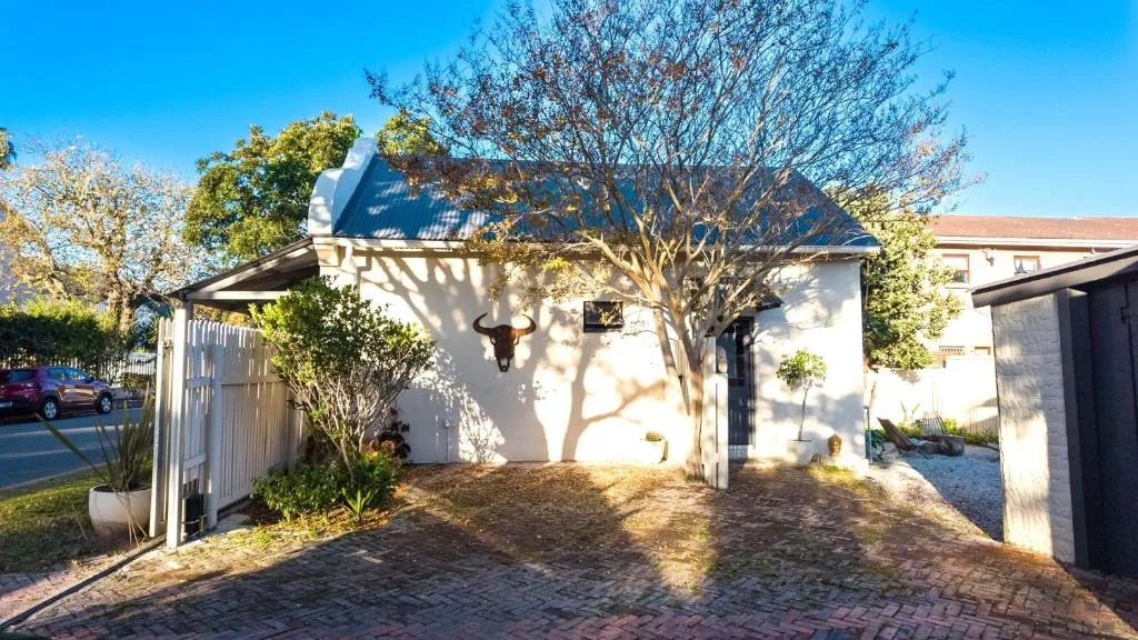 White cottage exterior with mature tree and brick driveway entrance