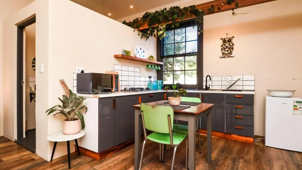 Modern kitchen with dark cabinetry, stove, microwave, and dining table with green chairs