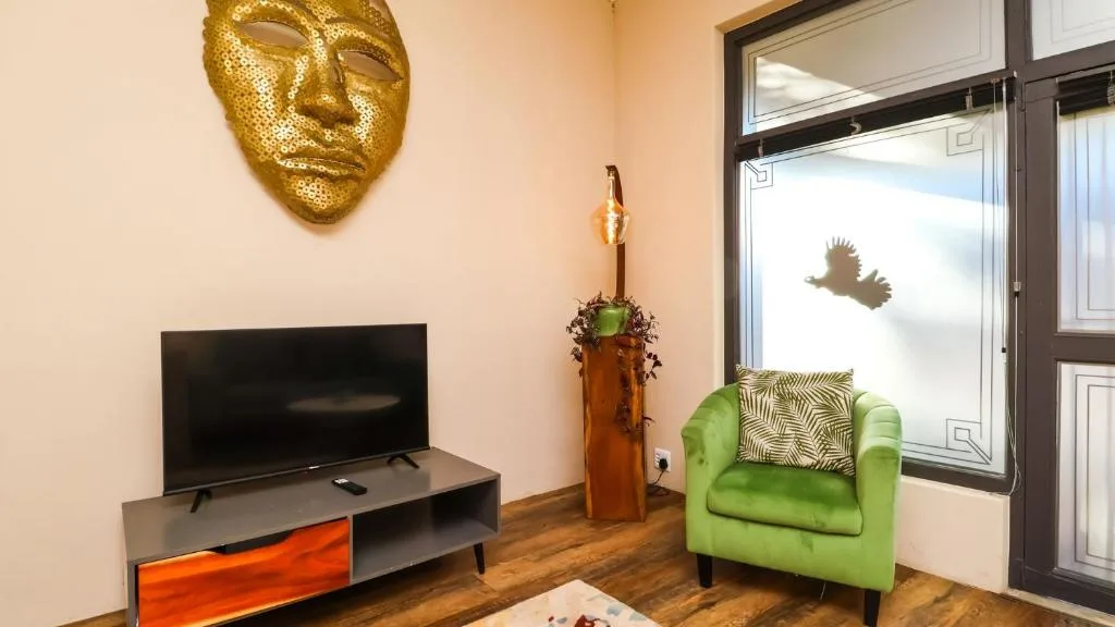 Bright lounge with green armchair, TV, and gold mask wall decor