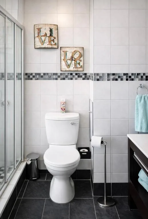 Clean white bathroom with toilet, shower enclosure, and decorative wall art