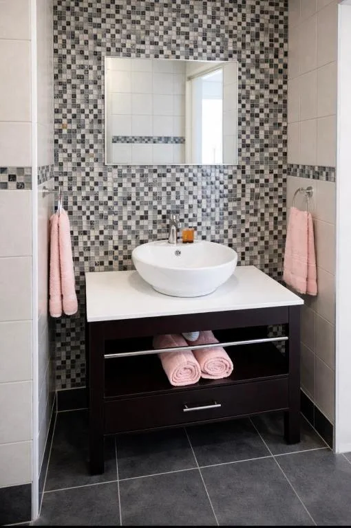 Modern bathroom with mosaic tile walls, round white sink, and black vanity