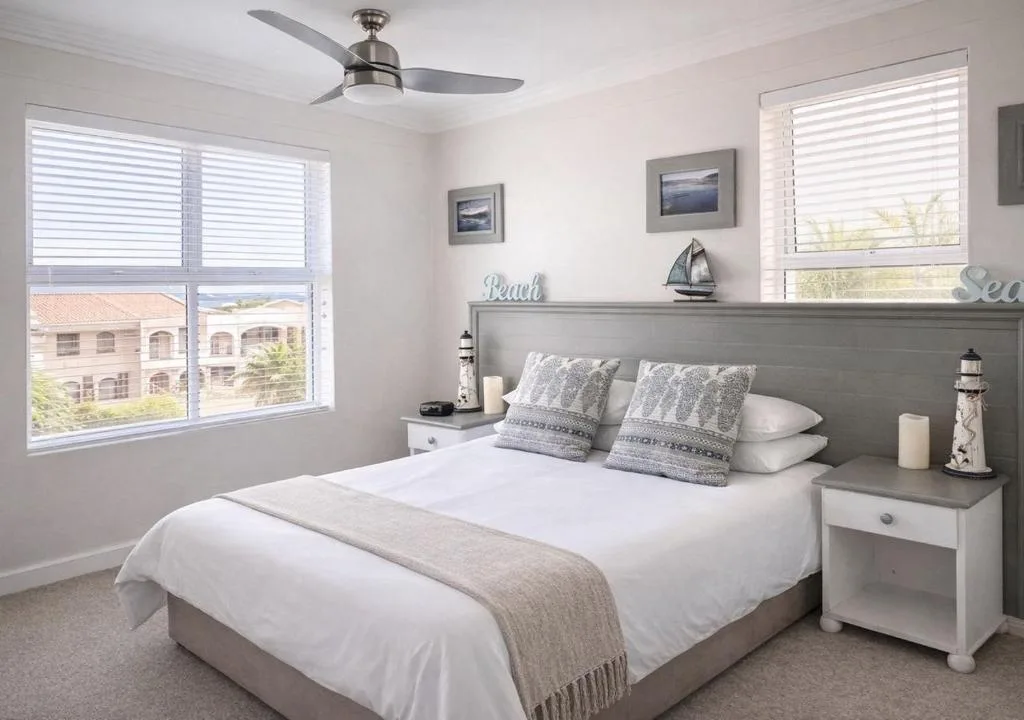 Coastal-themed bedroom with queen bed, gray headboard, and ocean views