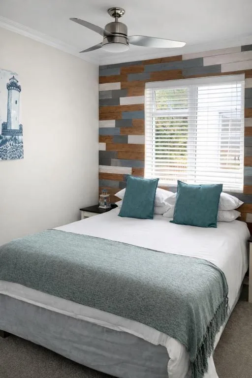 Modern bedroom with queen bed, teal cushions, wooden accent wall