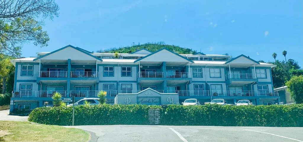 Modern blue apartment complex with balconies, hedges, and palm trees