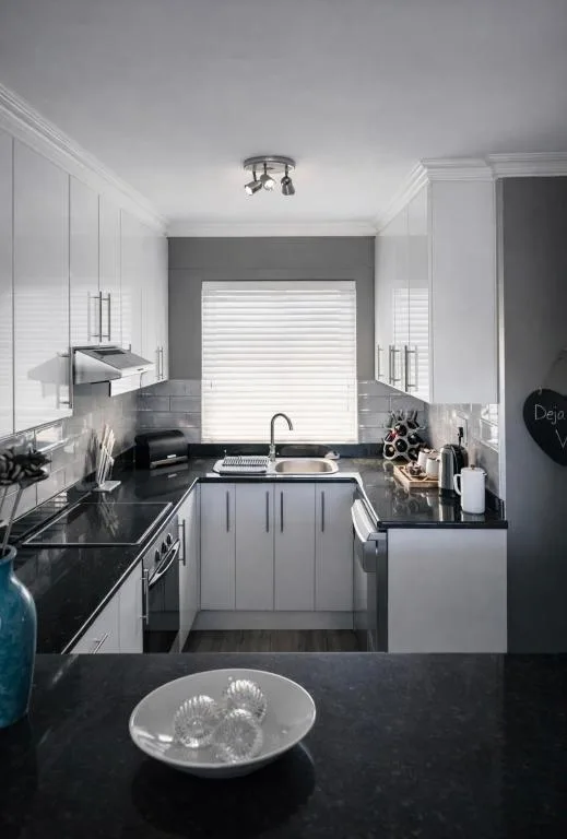 Modern kitchen with white cabinetry, black countertops, and window above sink