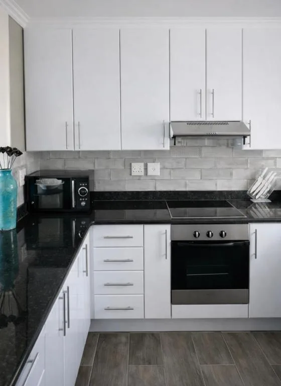 Modern white kitchen with black countertops, stainless steel appliances, and gray subway tile backsplash