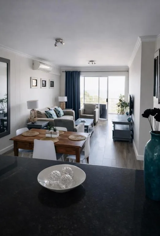 Open-plan lounge with gray sofa, dining table, large windows overlooking garden