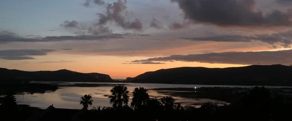 Sunset over Knysna Lagoon with mountains silhouetted against golden sky