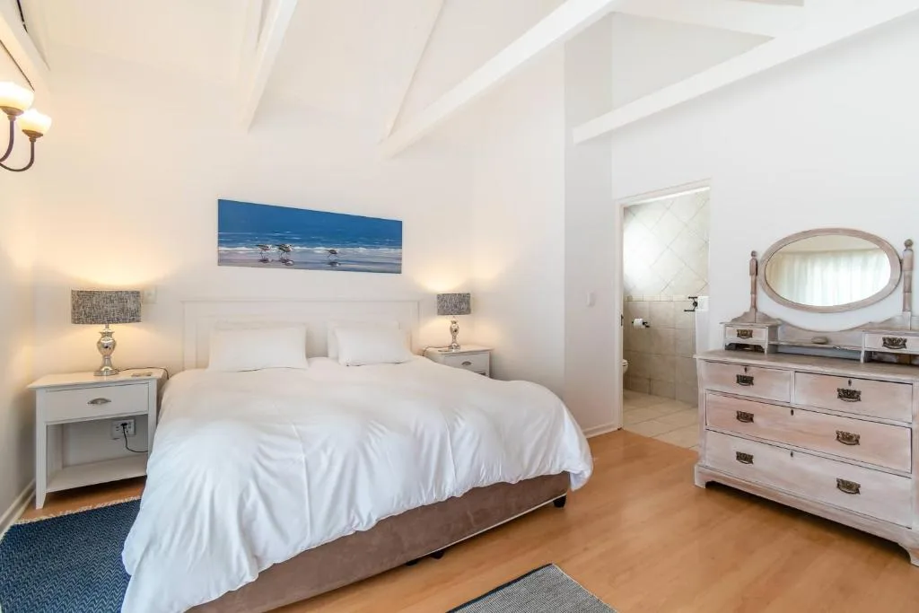 Bright bedroom with white bed, matching nightstands, and coastal artwork above headboard