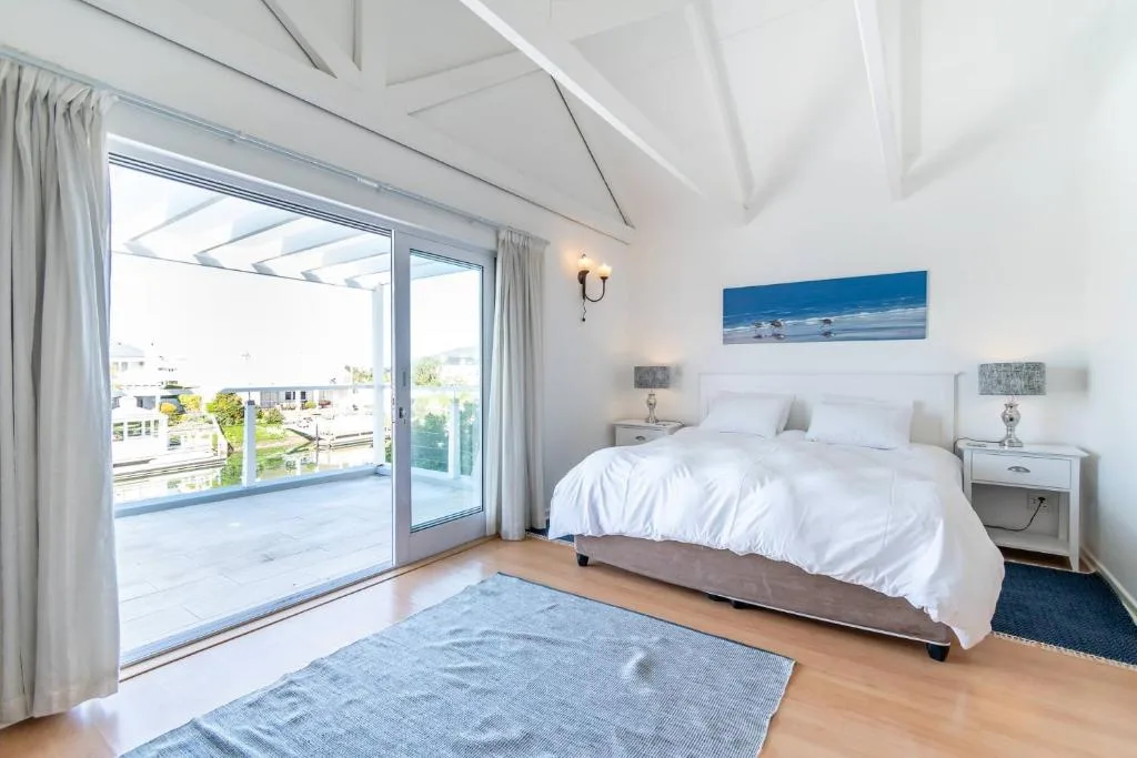 Bright modern bedroom with queen bed, deck access, and water views