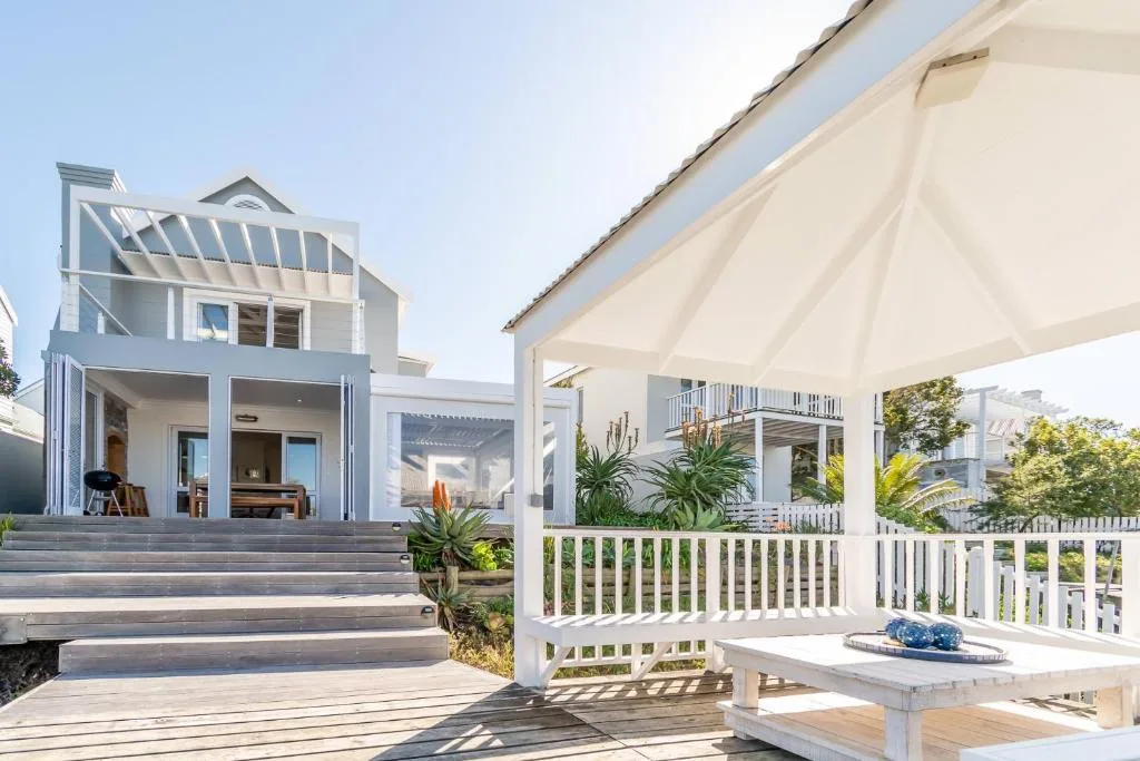 Shaded deck with white railings and cream umbrella overlooking modern home