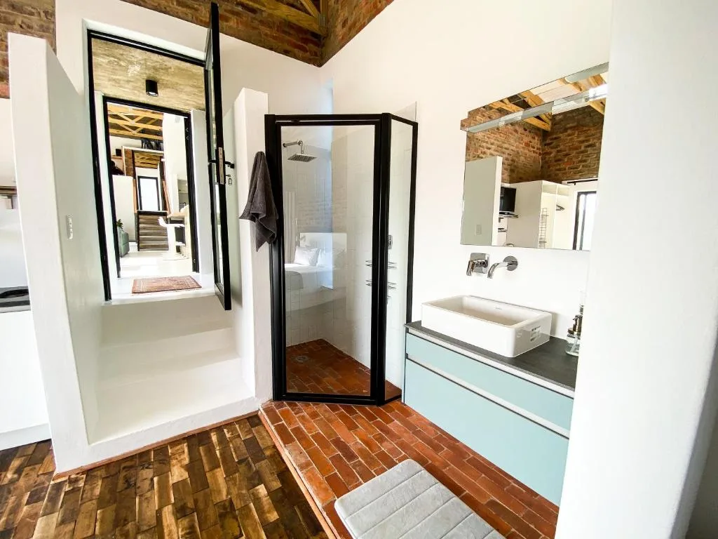 Modern bathroom with walk-in shower, vanity sink, and exposed brick ceiling