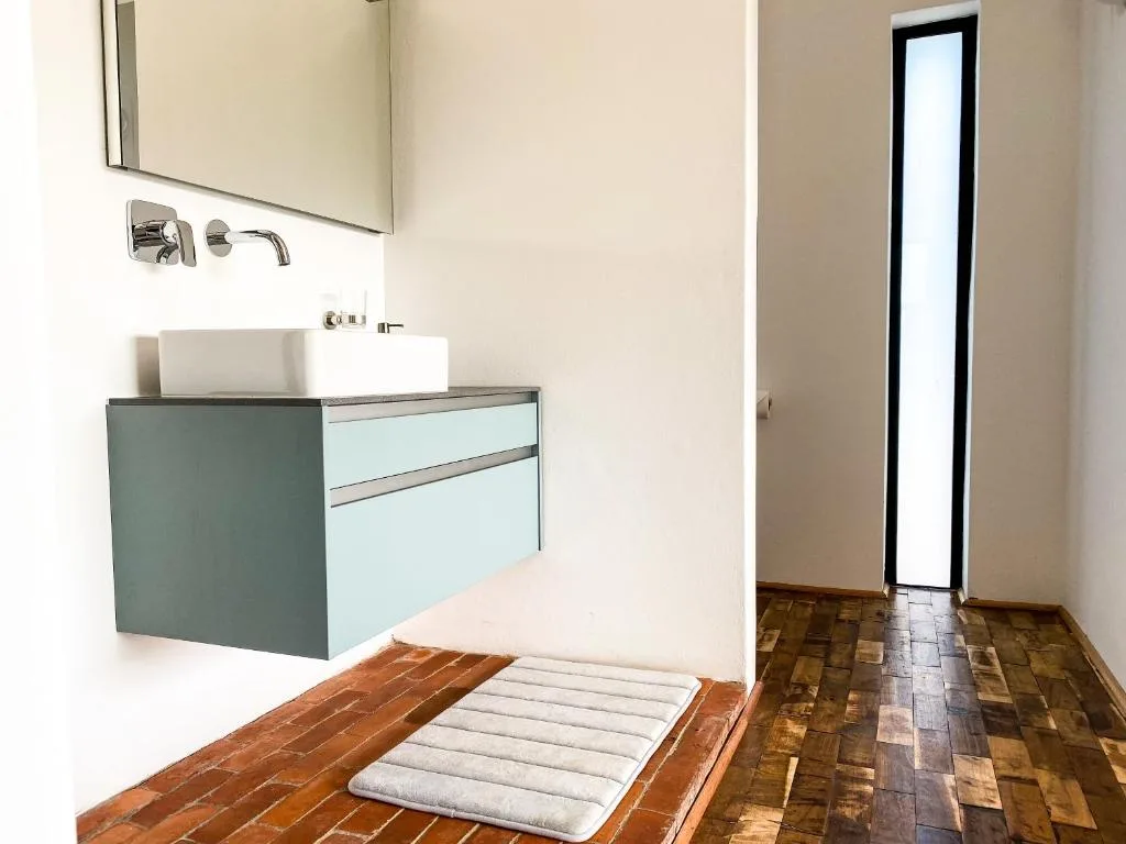 Modern bathroom with teal vanity, wall-mounted sink, and wooden flooring