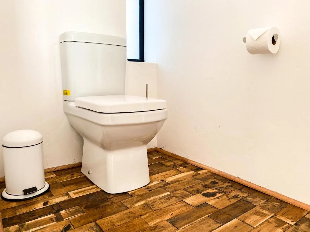 Clean bathroom with white toilet, pedal bin, and wooden floor