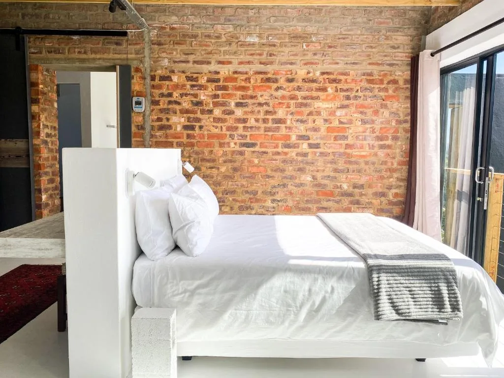 Modern white bed with crisp linens against exposed brick wall and glass doors