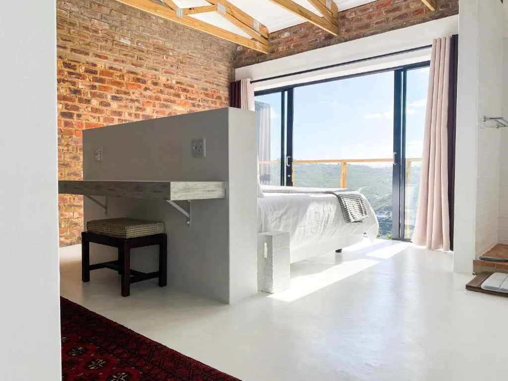 Modern bedroom with exposed brick walls, wooden beams, and panoramic garden views