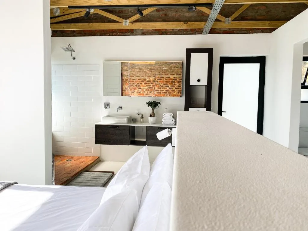 Modern bedroom with ensuite bathroom featuring exposed brick and wooden beams