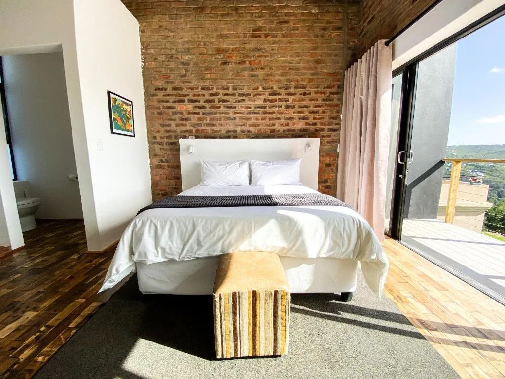 Bright bedroom with white bedding, exposed brick wall, wooden floors, and scenic view doors