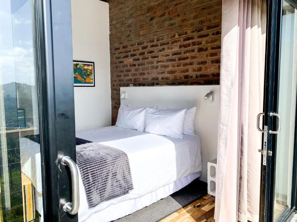 Modern bedroom with white bedding, exposed brick wall, large windows with mountain views