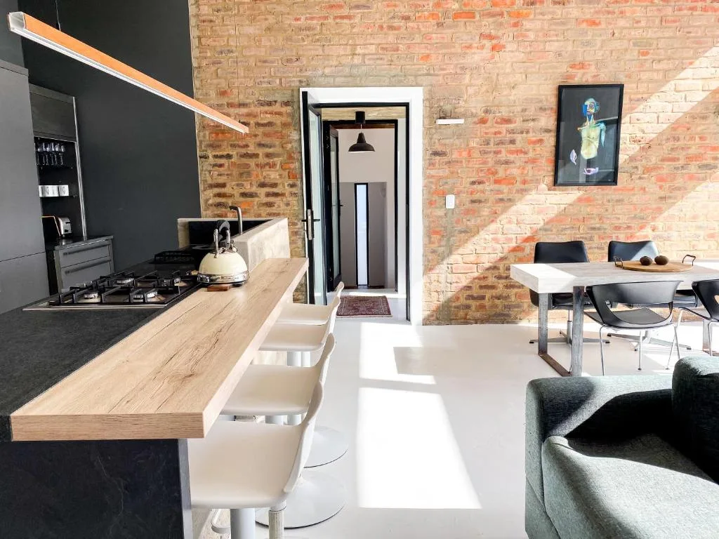 Modern open-plan kitchen with gas cooktop, exposed brick walls, dining area