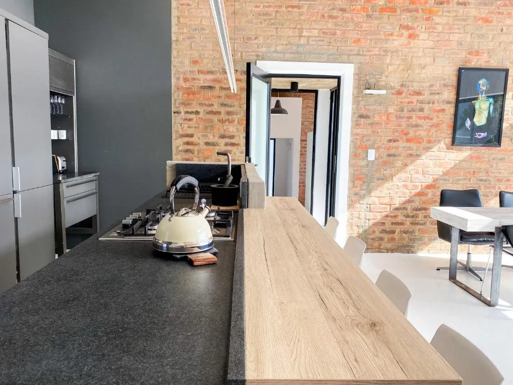 Modern kitchen with dark countertop, cream kettle, stove, and exposed brick wall