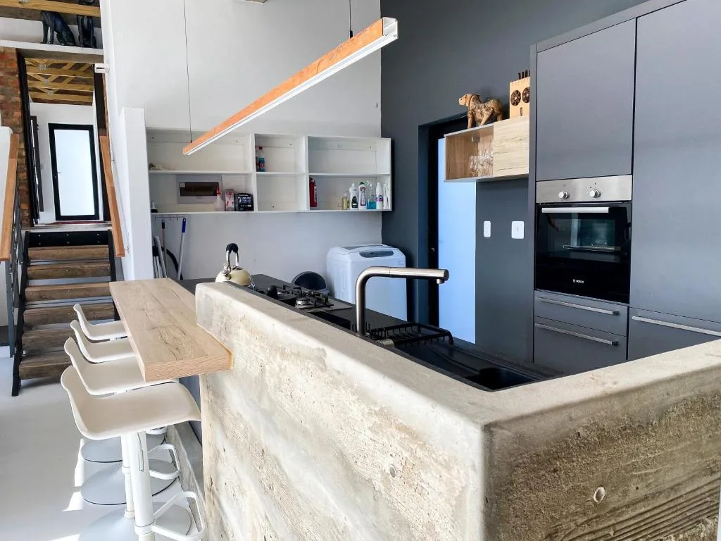 Modern kitchen with grey cabinetry, built-in oven, island counter, and wooden bar seating