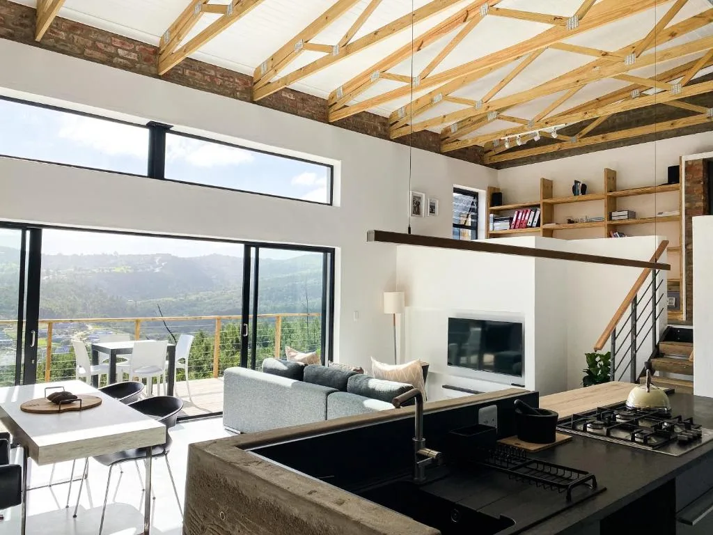Modern open-plan lounge with gray sofa, TV, and expansive mountain views through floor-to-ceiling windows