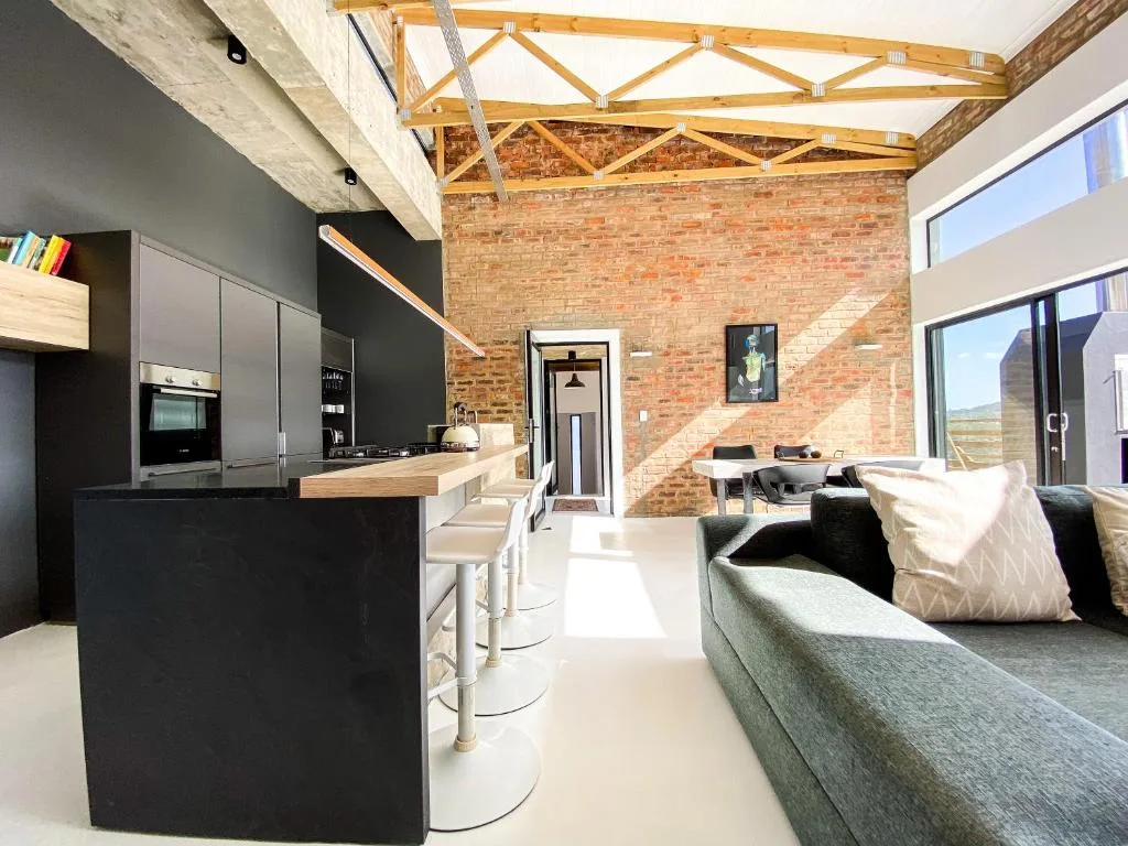Modern open-plan lounge with dark sofa, exposed brick, and contemporary kitchen island