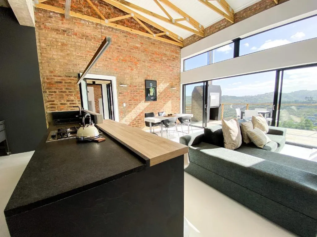Open-plan lounge with sofa, gas stove, and panoramic valley views through large windows