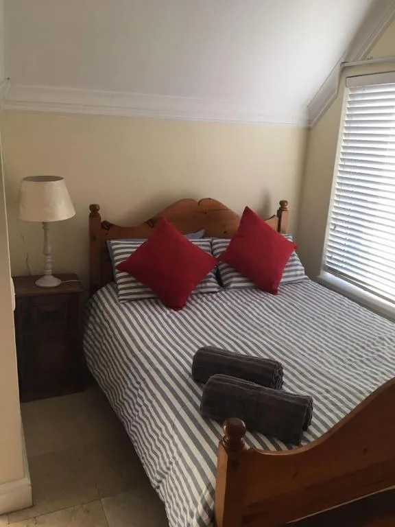 Bedroom with red cushions, striped bedding, wooden bed frame, and lamp