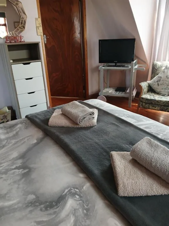 Bedroom with made bed, folded towels, TV, and wooden door