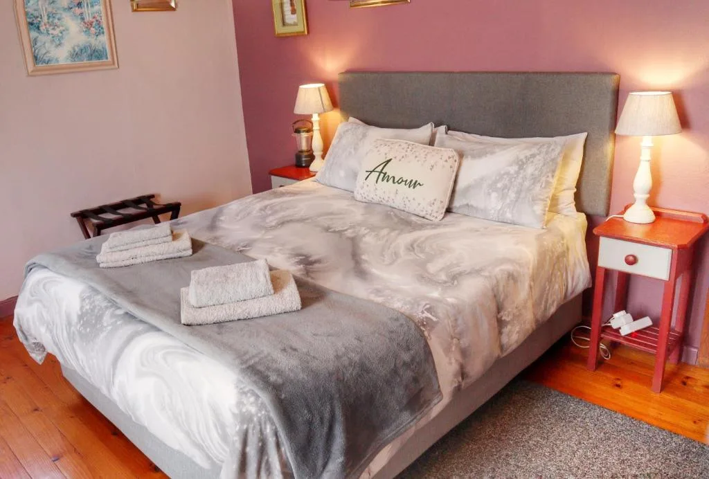 Spacious bedroom with gray upholstered bed, pink walls, and warm lighting